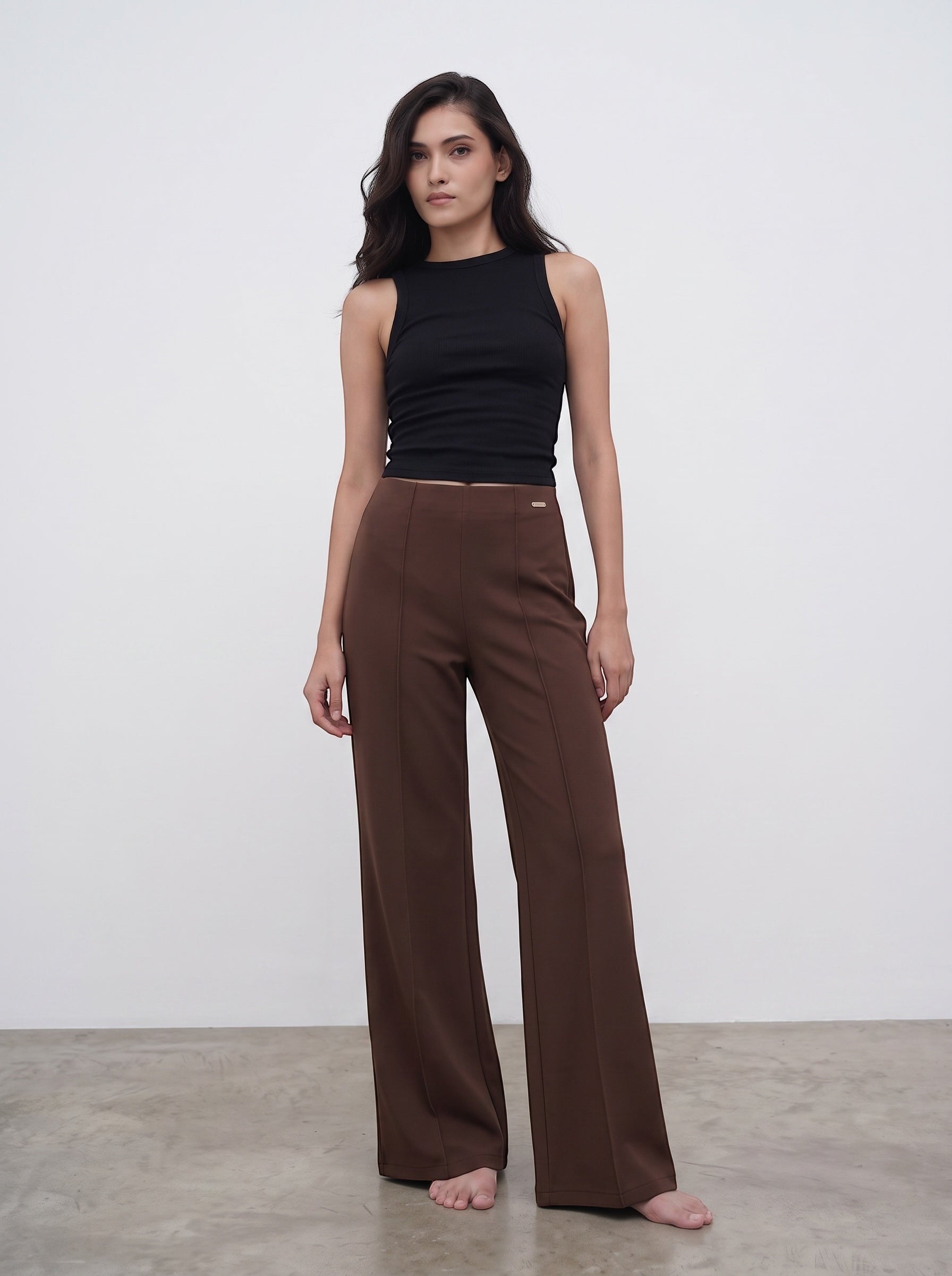 A model wearing duwies chocolate brown high-waisted wide-leg trousers with front seam detailing and a black tank top.